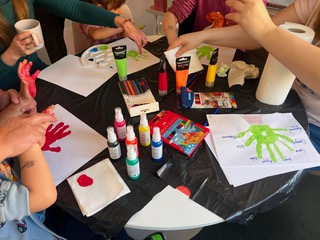 Kinder und Erwachsene gestalten gemeinsam bunte Handabdrücke im Familiensprachkurs.